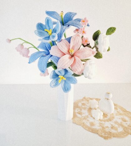 grand bouquet au crochet bleu et rose avec plusieurs lys bleus, un lys rose, petites fleurs roses et fleurs blanches dans un vase blanc